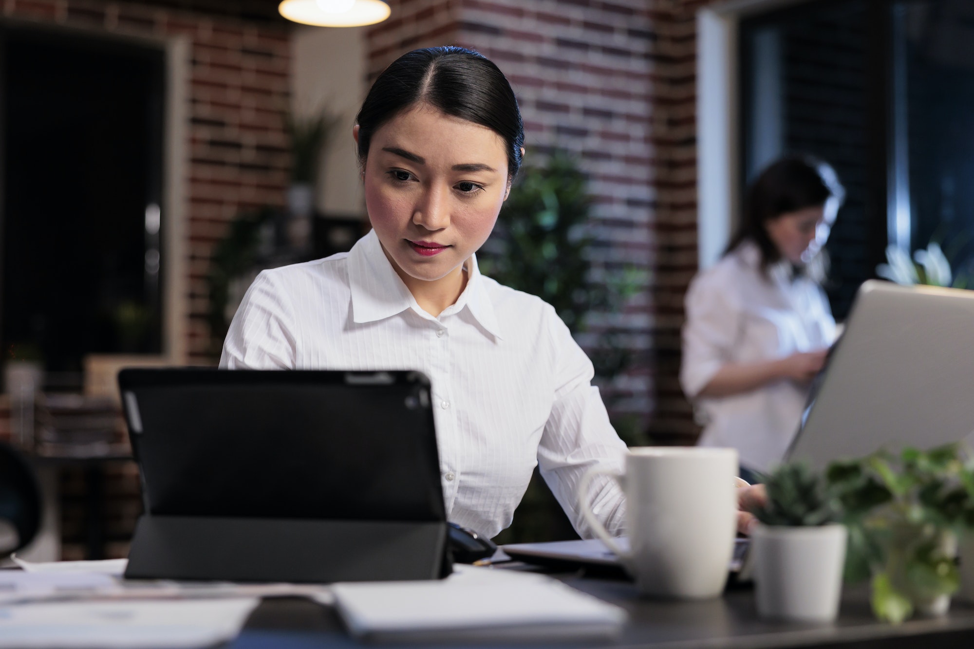 Asian businesswoman with modern tablet reviewing accounting documentation in office workspace