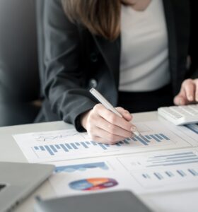 Close up of a businesswoman working in accounting using graphs and calculators at the office.